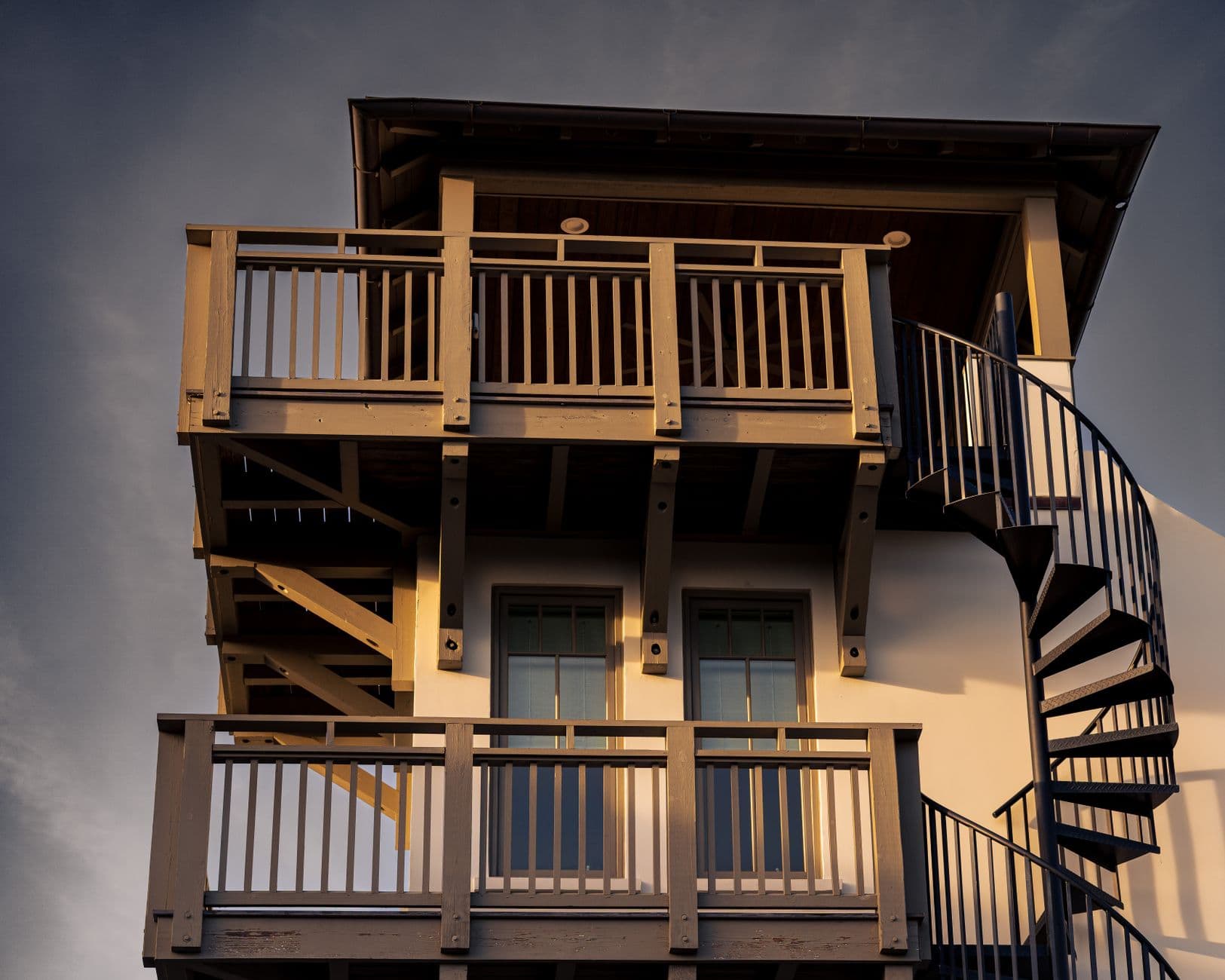 A rustic wooden balcony with a spiral staircase illuminated by warm sunset light.